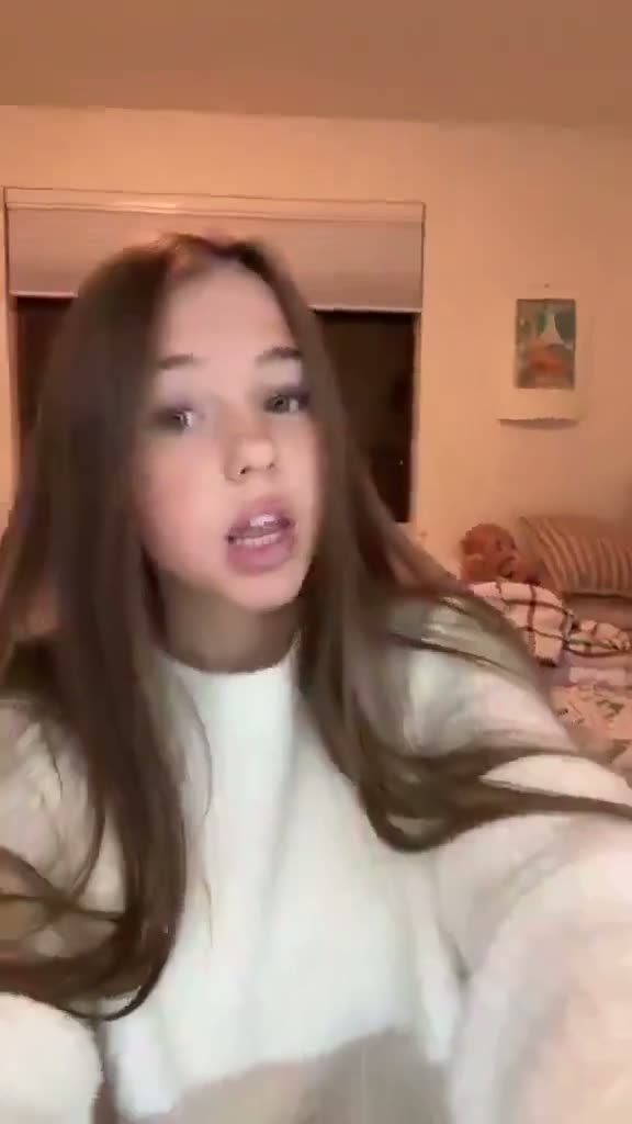 Brunette in a white top filming in a bedroom