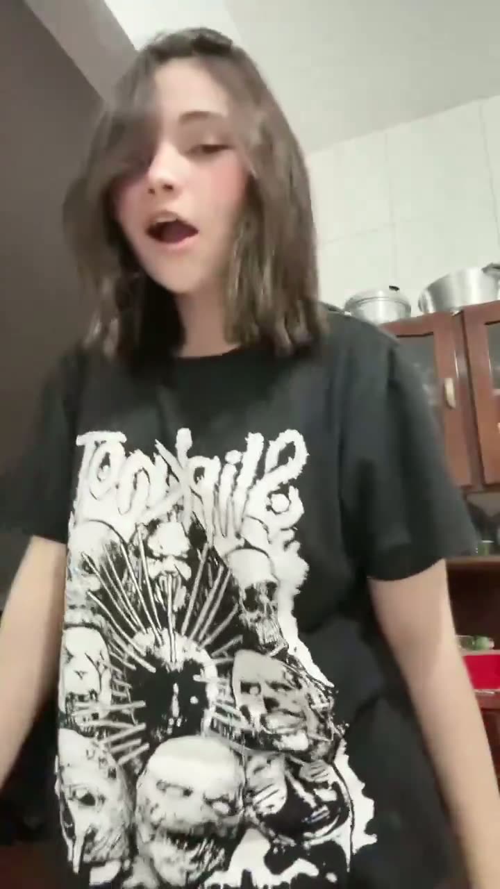 Brunette in a black band tee filming indoors