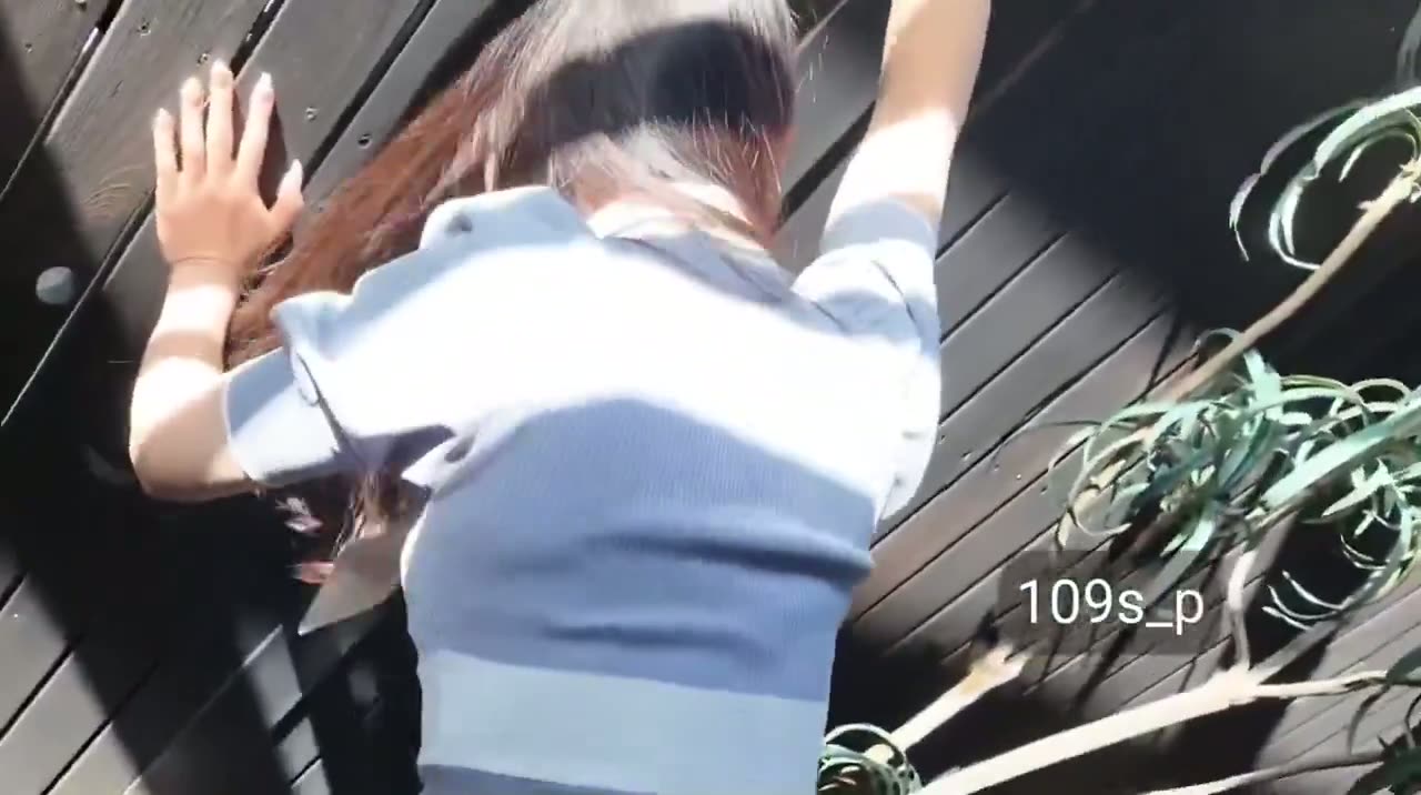 POV clip of a woman in a light blue top against a dark wall