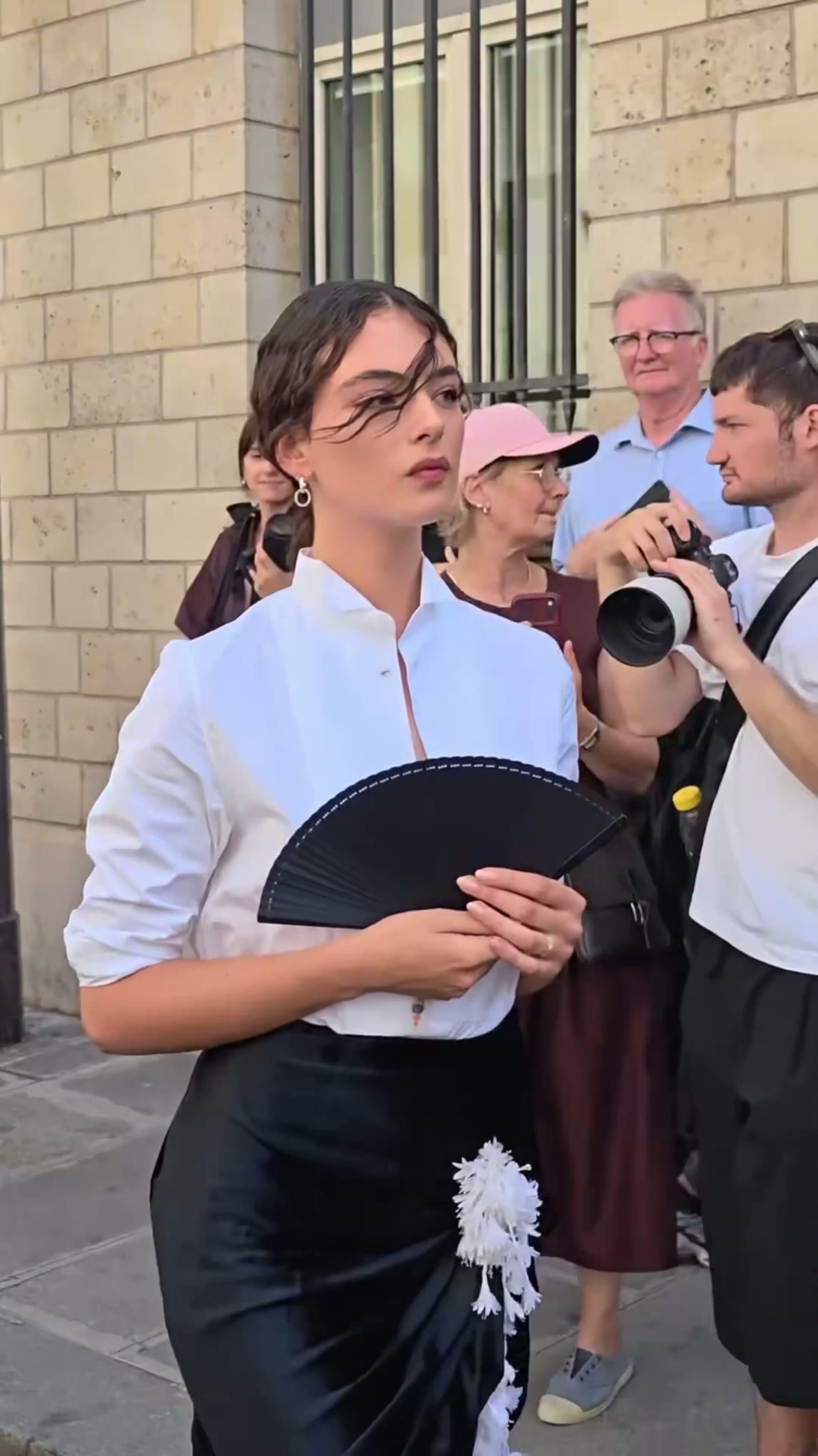 Woman in a white top and black skirt holding a fan on a street