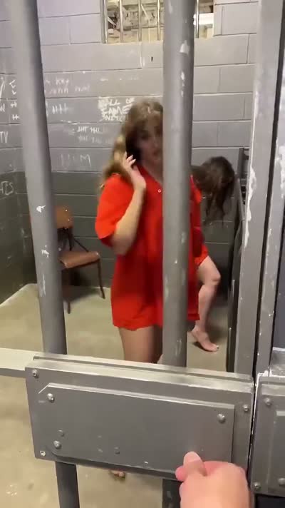 Redhead in an orange jail jumpsuit in a concrete holding cell