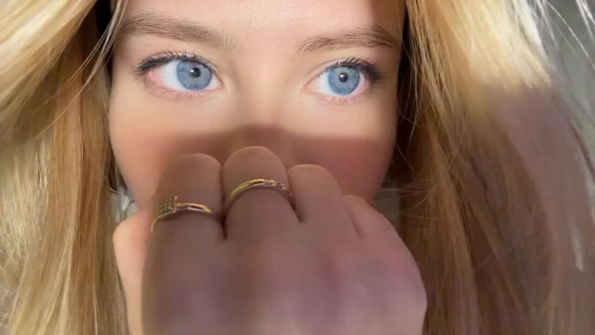 Close-up of a blonde with blue eyes covering her mouth (@zoomerdarlings)