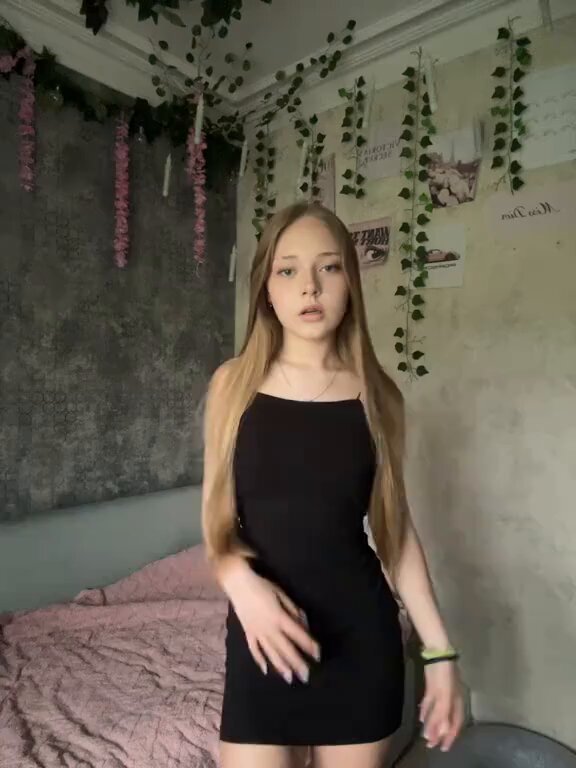 Blonde in a black mini dress in a bedroom with hanging vines (@Carolinemaryros)