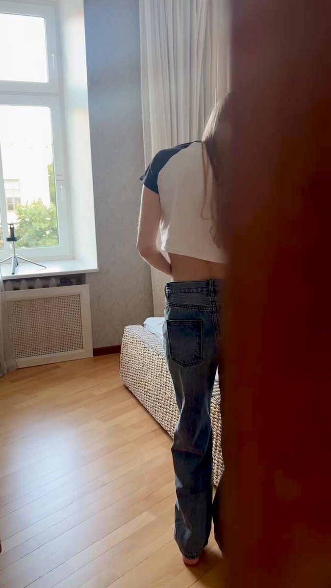Brunette in a white-and-black raglan crop top and wide-leg jeans by a window (@MuhammadLu52052)