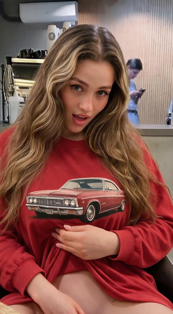 Blonde with long waves in a red vintage-car sweatshirt in a cafe