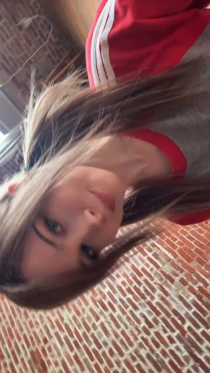 Blonde in a red track jacket on brick