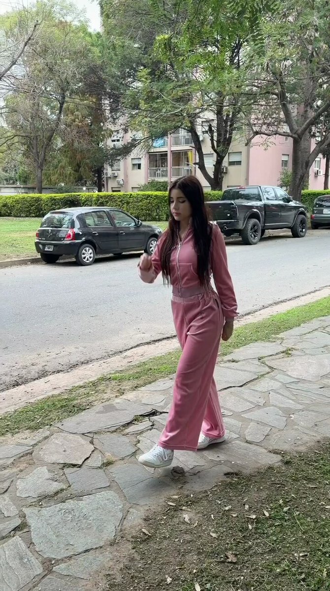 Brunette in a pink tracksuit walking on a sidewalk (@JuanitaBowle)