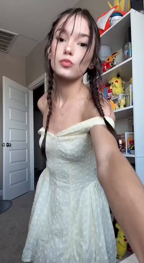 Brunette in a white dress by a Pokemon shelf (@TrinaTheory_)